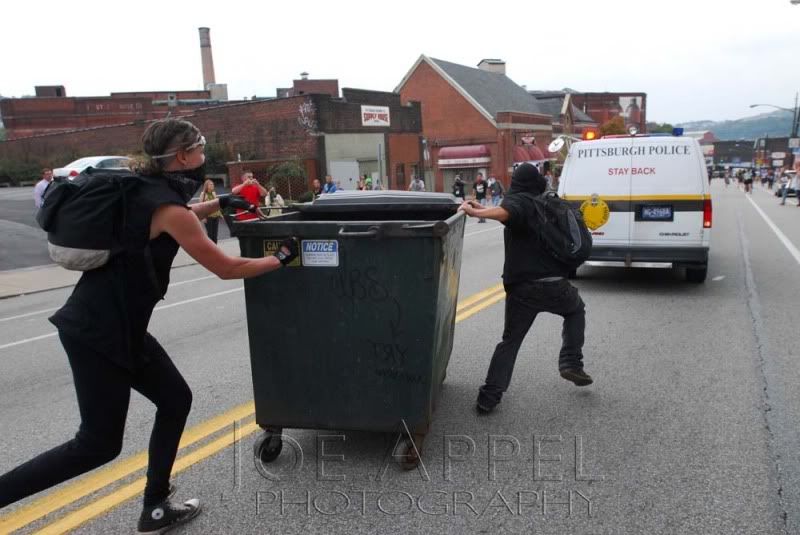 Anarchists chase a police van with a dumpster.